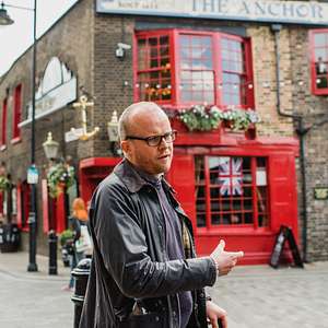 A guide gestures while leading a tour outside The Anchor pub with Union Jack in the window.