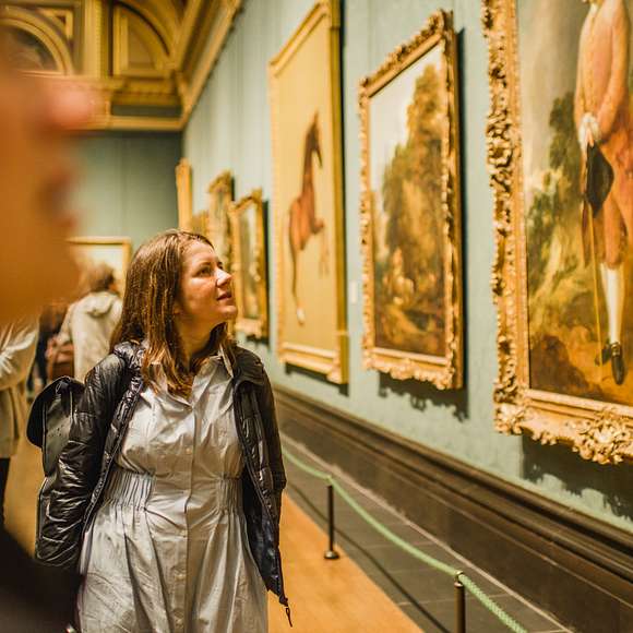 Visitor admiring a series of framed paintings in a richly decorated gallery room at the National Gallery.