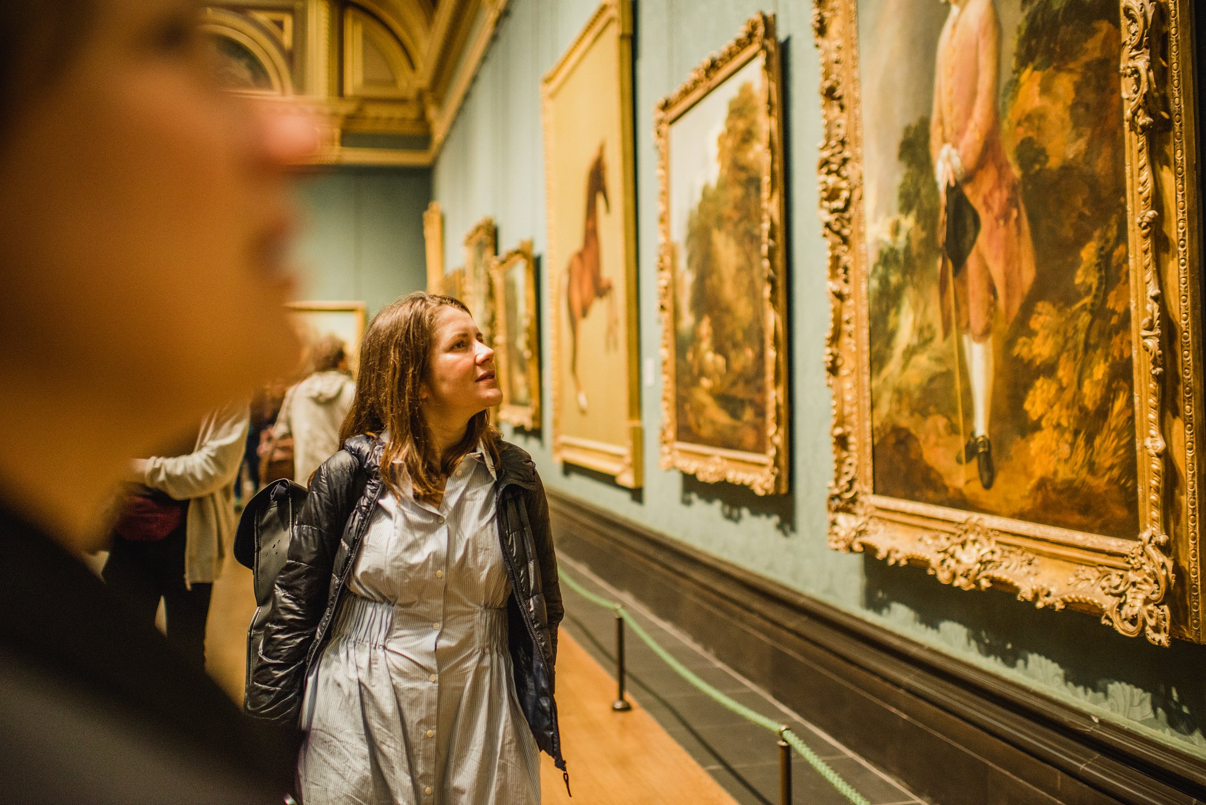 Visitor admiring a series of framed paintings in a richly decorated gallery room at the National Gallery.