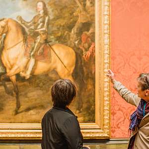 Tour guide gesturing toward a grand equestrian portrait while discussing it with a guest inside the National Gallery.