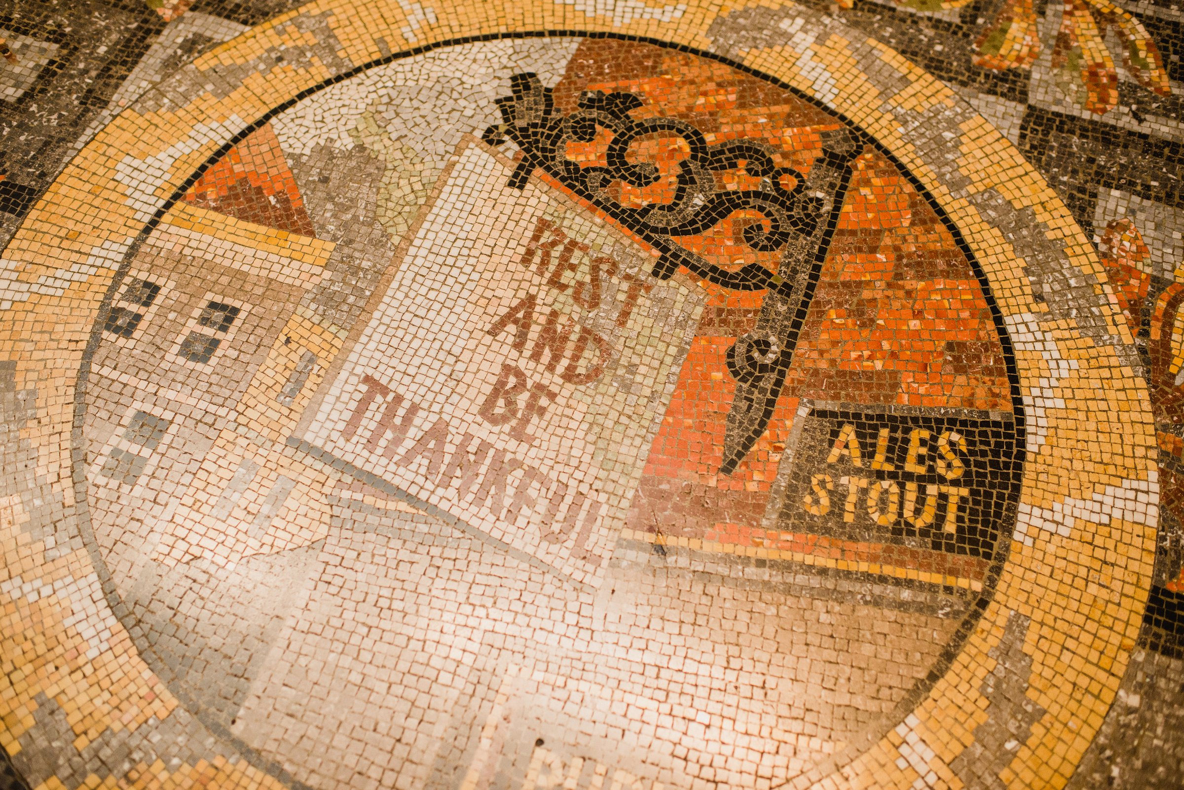 Mosaic tile floor at the National Gallery reading “Rest and Be Thankful” with decorative patterns and signage.
