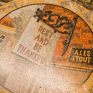 Mosaic tile floor at the National Gallery reading “Rest and Be Thankful” with decorative patterns and signage.