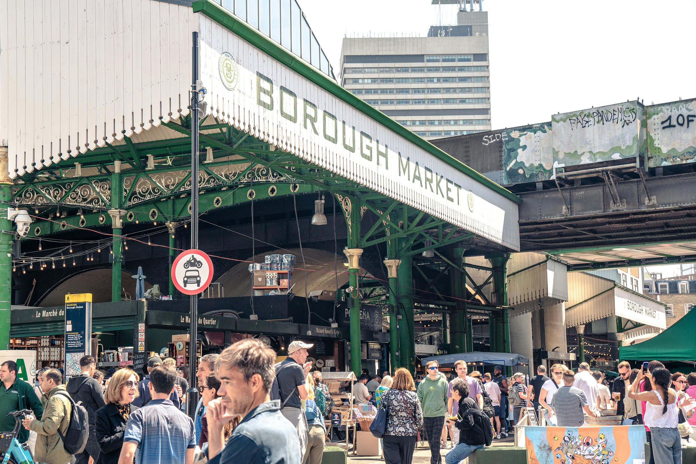A bustling crowd gathers outside Borough Market on a sunny day, surrounded by street signs and market stalls.