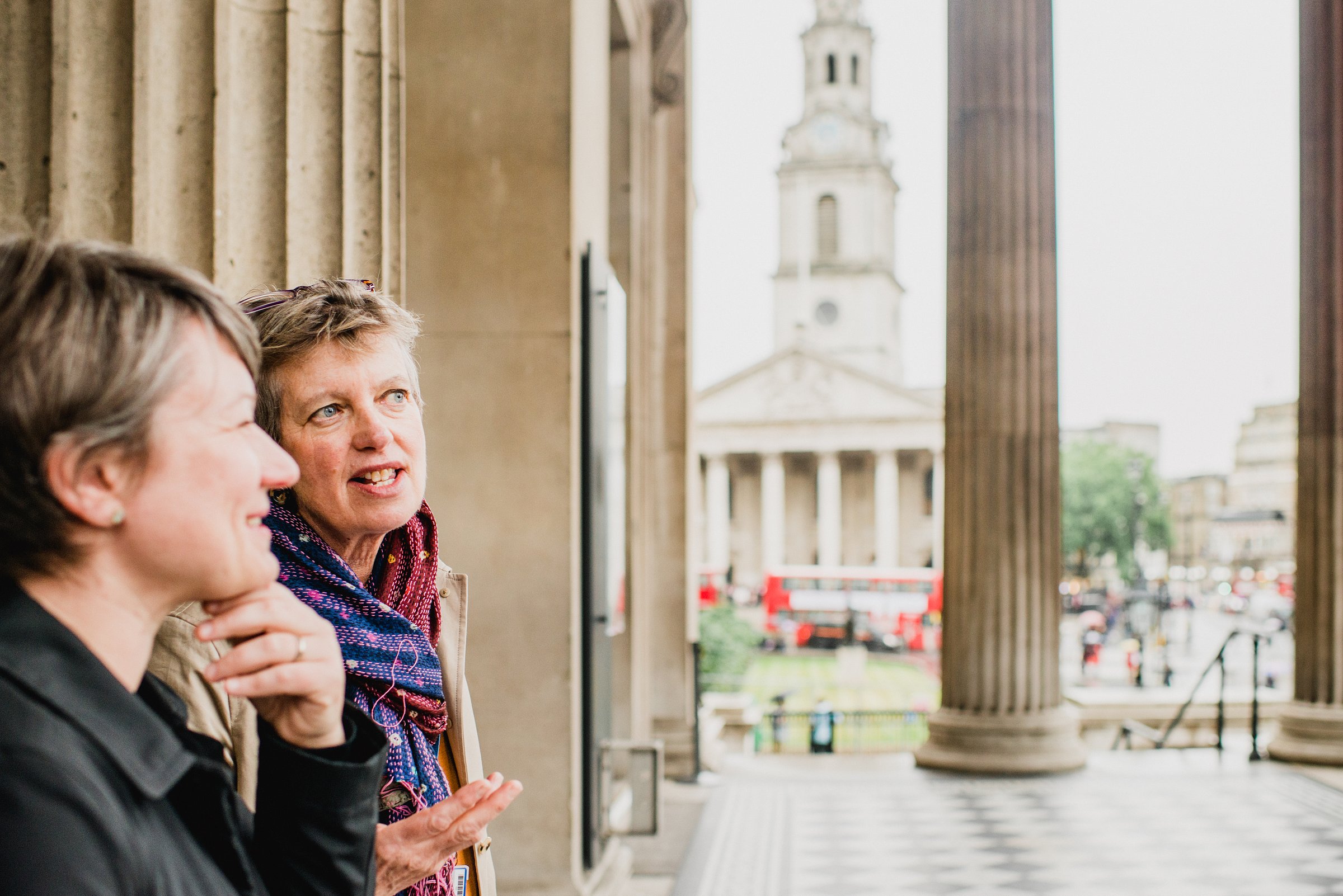 Two women talk with columns of the National Gallery behind them and St. Martin-in-the-Fields church in the distance.