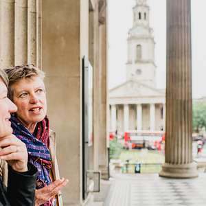 Two women talk with columns of the National Gallery behind them and St. Martin-in-the-Fields church in the distance.