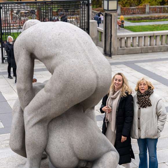 Two women admire granite statues in Vigeland Park on a cool autumn day.