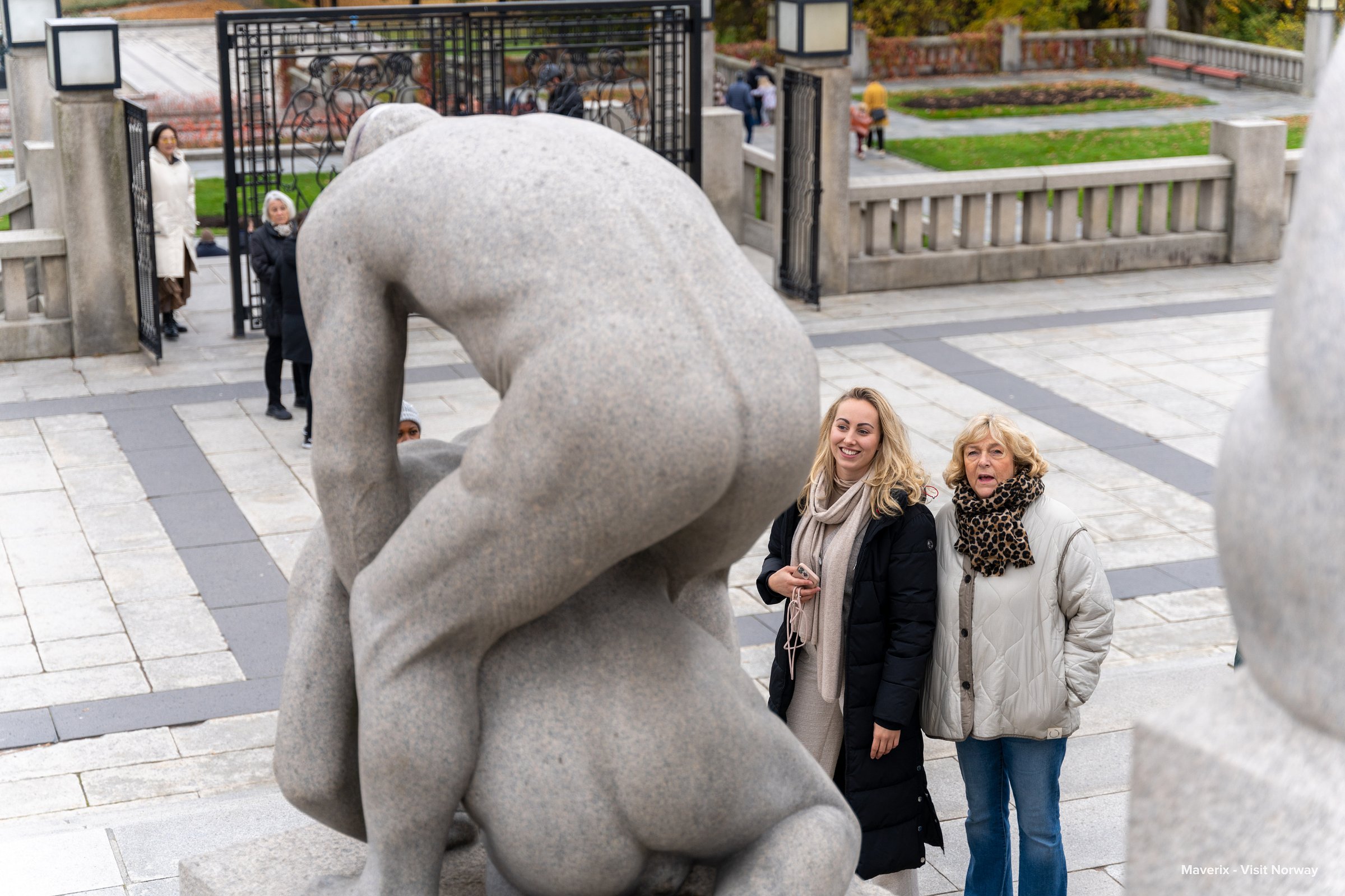 Two women admire granite statues in Vigeland Park on a cool autumn day.