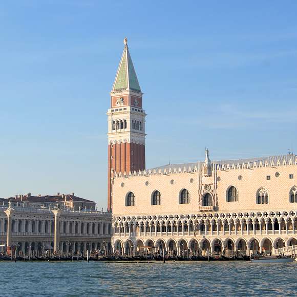 Panoramic view of the Doge's Palace and Campanile di San Marco from the water, showcasing Venice’s iconic architecture against a clear blue sky.
