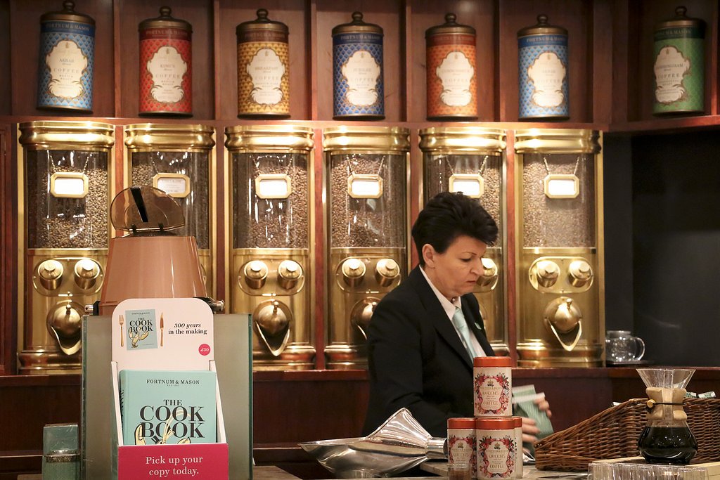 Staff member at a specialty tea and coffee counter in Fortnum & Mason, with decorative tins and grinders behind her.