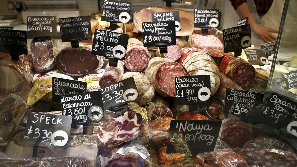Display of artisanal cured meats with handwritten price tags at a deli counter during a London food tour stop.