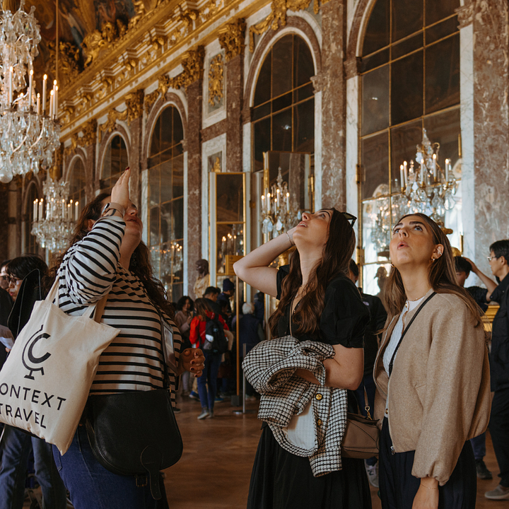Two guests look up at a detail pointed out by their guide in the Hall of Mirrors in Versailles