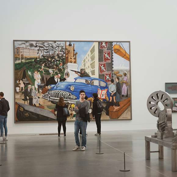 Visitors viewing a large industrial-themed painting and modern sculptures inside a spacious gallery at Tate Modern.