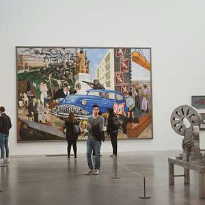 Visitors viewing a large industrial-themed painting and modern sculptures inside a spacious gallery at Tate Modern.