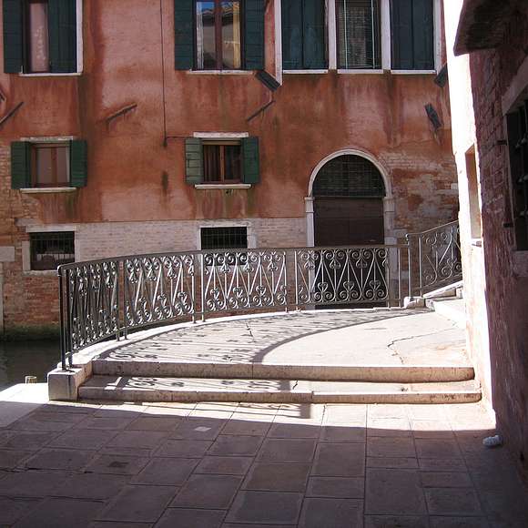 A charming iron bridge crosses a narrow canal in a quiet Cannaregio courtyard.