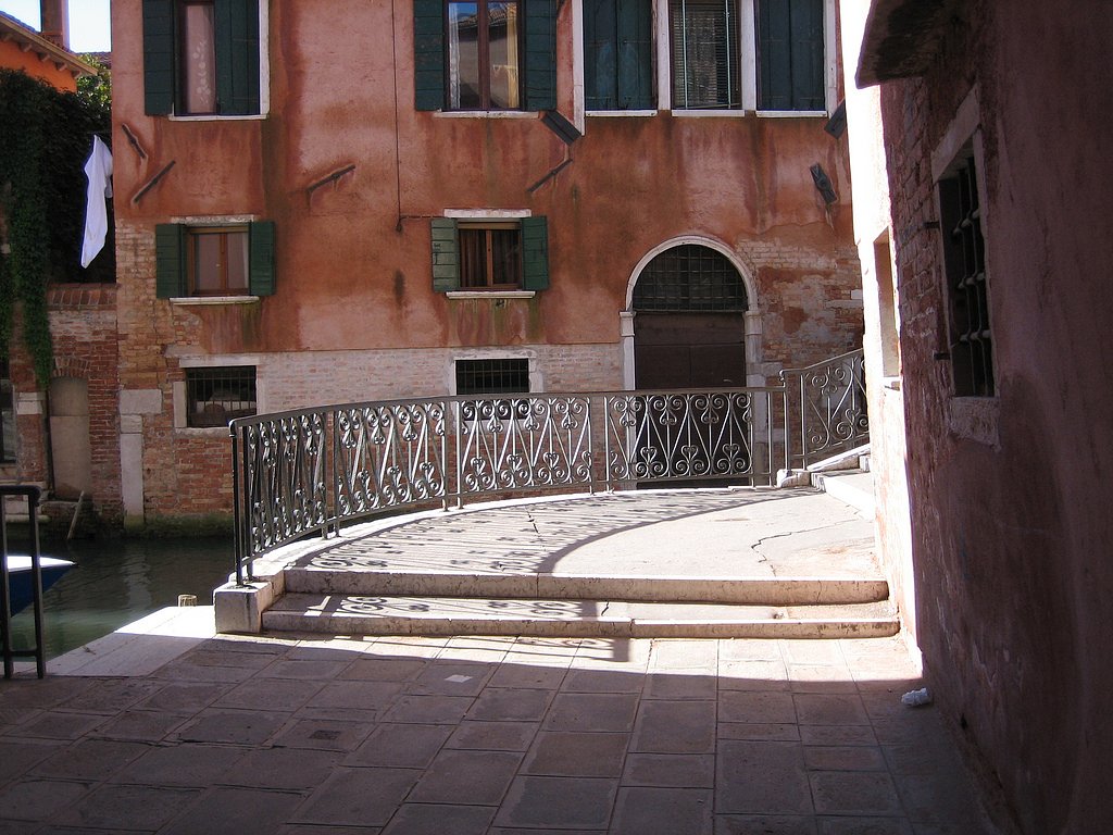 A charming iron bridge crosses a narrow canal in a quiet Cannaregio courtyard.