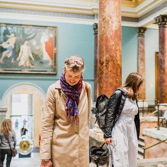 Two women ascending a grand staircase inside the National Gallery, surrounded by marble columns and classical art.