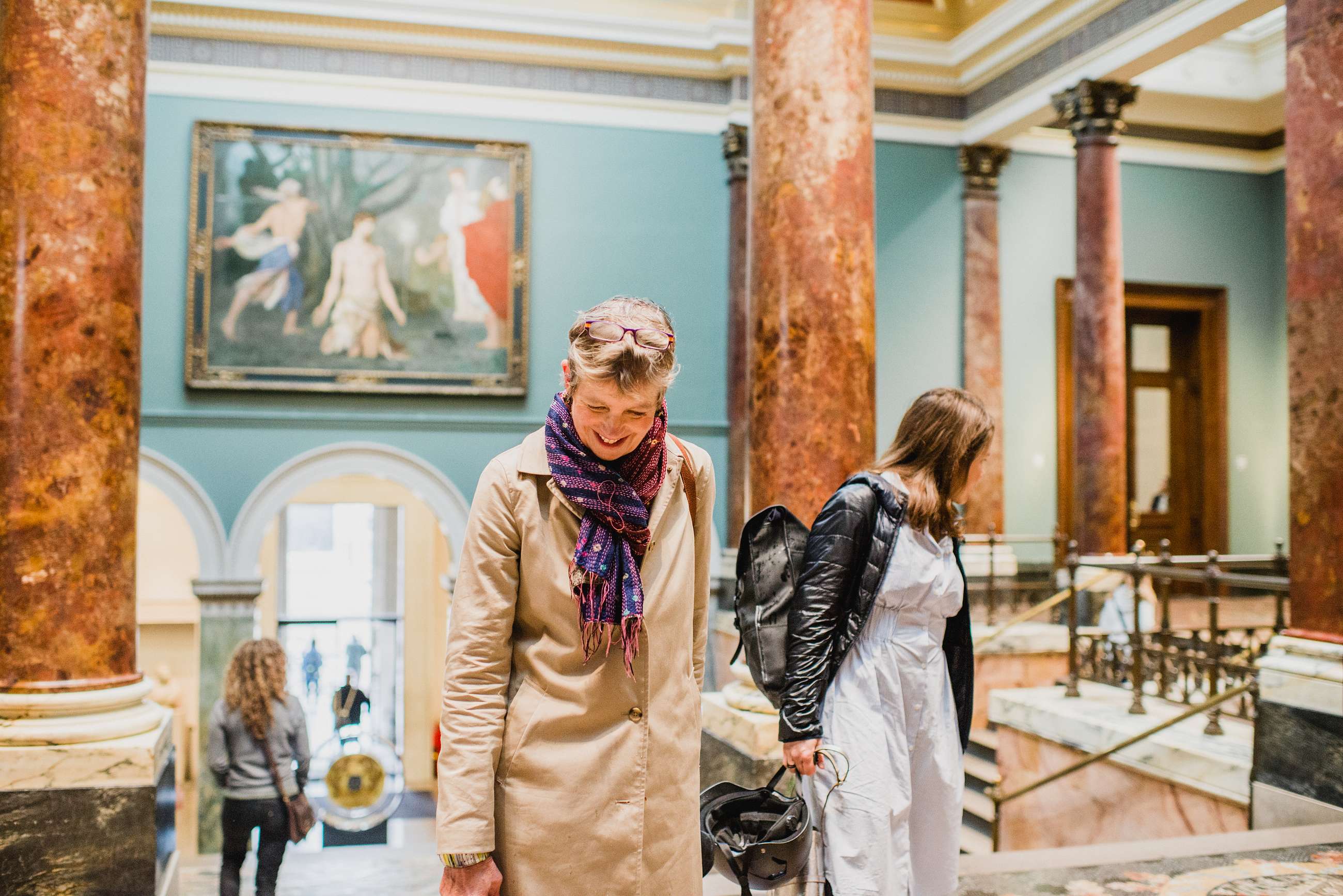 Two women ascending a grand staircase inside the National Gallery, surrounded by marble columns and classical art.