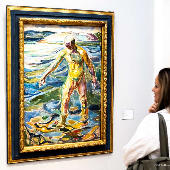 A woman observes a colorful framed painting of a figure standing in water.